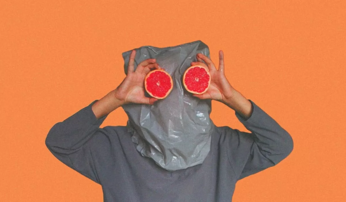 person head covered in plastic bag holding 2 oranges at eye level