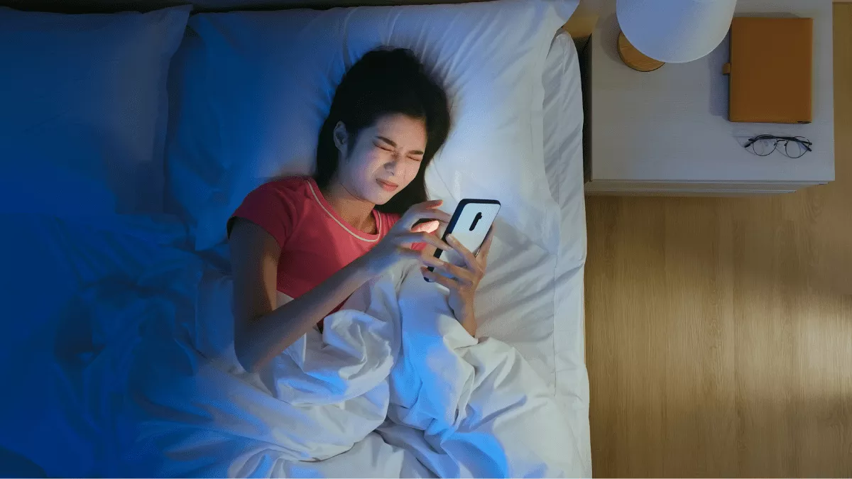 woman squinting at smartphone screen in bed